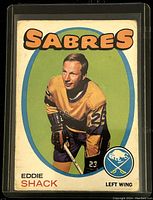 Front view of 1971-72 O-Pee-Chee hockey card featuring Eddie Shack of the Buffalo Sabres in yellow jersey with green background and team name.