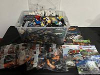 Large plastic storage bin filled with assorted loose LEGO pieces, front view showing manuals and sealed bags laid out in front