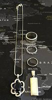 Sterling silver necklace with black stone pendant and three silver rings laid out on a map background, clear view of chain and pendant details.