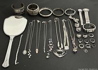 Overview of all silver-tone jewelry items and handheld mirror on black background