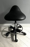 Front angle of the ergonomic black ergonomic saddle stool showing the saddle seat and base with caster wheels and footrest ring