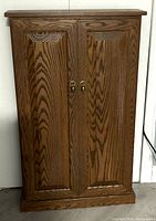Front view of closed wooden cabinet with two paneled doors and brass handles.