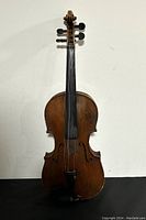 Front view of aged wooden violin missing most strings, showing fingerboard, tailpiece, and chin rest.