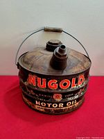 Front angle view showing round metal oil can with rust and paint wear, and original handle, filling cap, and spout without cap.