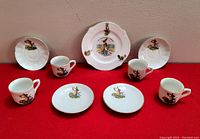 Full set of 4 cups, 4 saucers, and 1 small plate with rabbit theme shown on red background against beige wall.