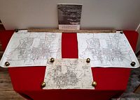 Wide shot of the lot showing the Planning Study book upright behind two large identical maps pinned on a red background with a smaller map pinned in front, and wooden yardstick above maps.