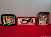 Three different 1990s Coca Cola metal advertising trays displayed side by side, showing various images and styles.
