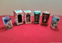 Five Disney movie collector glasses in a row with four original boxes behind them, showing the colorful artwork and packaging from Burger King's 1994 promotion.