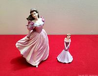 Two Coalport porcelain figurines on red cloth background, one about 9 inches tall, the other smaller.