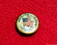 Front image of the pinback showing the American flag and 'PERSONAL LIBERTY LEAGUE' text on a cream background with soiling.