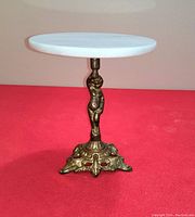 Front angle view of the vintage brass and marble figural plant or lamp stand showing the marble top and figural brass support.