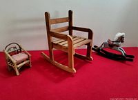 Photo of all three items together on a red surface: the rocking chair, folk art doll chair, and rocking horse.