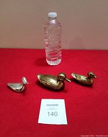 Three small duck sculptures displayed on a red cloth with a water bottle for scale, showing their relative sizes and finishes.