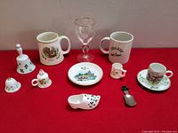 Photo of assorted vintage Irish pottery and dish items on red background showing mugs, bells, small plate, glass, and small shoe item