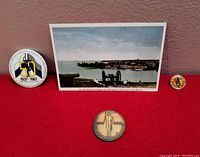 Four items laid out on a red background: the 1976 anniversary medallion, the Vimy Barracks pin, the Paladins lapel pin, and the unused postcard featuring a view of RMC from Fort Henry.