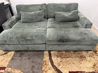 Front view of the green corduroy sleeper sofa with two matching toss pillows placed on a patterned rug.