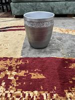 Photo shows silver cylindrical bathroom garbage can with brushed metal finish and a glittery decorative band around the top.