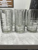 Photo showing three large crystal glass tumblers with geometric cut patterns arranged on a speckled countertop under soft lighting.