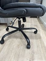 Close-up side view of the chair base and adjusting lever showing five caster wheels and tilt control knob.