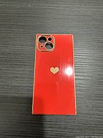 Front view of the red iPhone 14 case with gold edges and a centered gold heart design on the back.