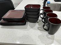 Photo of stacked maroon and brown square dinnerware including plates, bowls, and mugs on a kitchen counter
