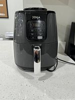 Front view of the grey Ninja air fryer on a countertop showing digital control panel and basket handle.