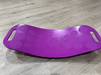 Photo of purple plastic curved ab twist board with handles, lying on wooden floor, showing textured grip surface.