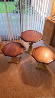 Full view of three varying size wooden end tables with octagonal tops arranged on carpet near glass door and dresser.