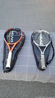 Two Head tennis rackets with black covers displaying logos, on a checkered cloth backdrop.