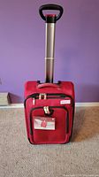 Front view of red 4 wheel carry-on luggage with extended telescoping handle, showing the suitcase upright on the floor.
