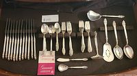 Full set of silverware laid out on black background showing forks, spoons, knives, and serving utensils with Community Silverplate label and guarantee card.