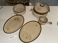 Photo of Dutch oven with lid, gravy float, two large oval serving plates, and one large serving bowl in beige Denby Memories stoneware pattern.