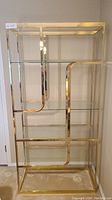 Front view of open-frame brass-finished metal shelf with four glass shelves