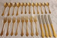 Photo showing all 21 pieces of Towle gold electroplated cutlery arranged: 8 spoons, 8 forks, and 5 knives on a white patterned tablecloth.