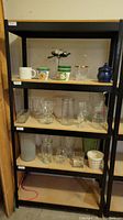 Front view of the black metal storage rack with wooden shelves holding various glassware and cups (contents not included).