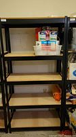 Full view of the metal storage rack with five wooden shelves. Some household items are on one shelf but not included in sale.