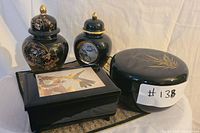 Set of black ceramic and pottery decorative items with gold floral and bamboo motifs including ginger jars, a round box, and a rectangular box.