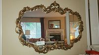 Front view of the ornate gold framed mirror reflecting living room with fireplace.