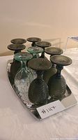Silver rectangular serving platter with seven dark green hobnail goblets and one smaller green goblet upside down on the platter.