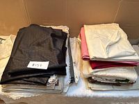 Two stacks of folded table linens including tablecloths and placemats in black, white, pink, red, and off-white colors, displayed on a table.