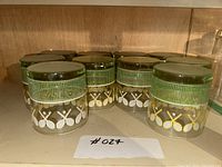 Ten clear drinking glasses arranged on a shelf, each decorated with tennis rackets and a green grid pattern.