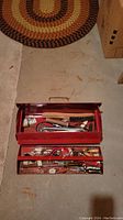 First photo showing open red metal toolbox with two trays filled with assorted hand tools laid out on floor.