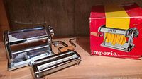 Pasta machine fully assembled on wood surface with original red and yellow Imperia box in background.