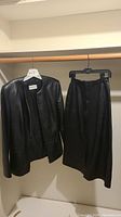 Photo of black leather jacket and skirt hanging on hangers in closet