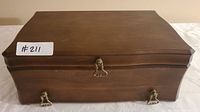 Closed wooden jewelry box showing smooth brown finish with brass handles and clasps.