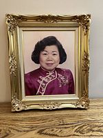 Front view of a gold-colored ornate frame containing a portrait photo of a woman, showing frame detailing and overall condition