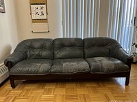 Full front view of the three-seat leather sofa showing entire piece with wood frame and dark leather cushions.