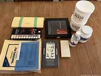 Photo showing all supplied items including pencil sets, paint palettes, gesso jars and sanding pads on wood table surface.