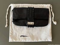 Black leather clutch purse resting on white drawstring dust bag with '3.1 Phillip Lim' embroidered branding