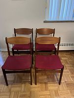 Front view of all four teak chairs showing red upholstered seats and curved backrests